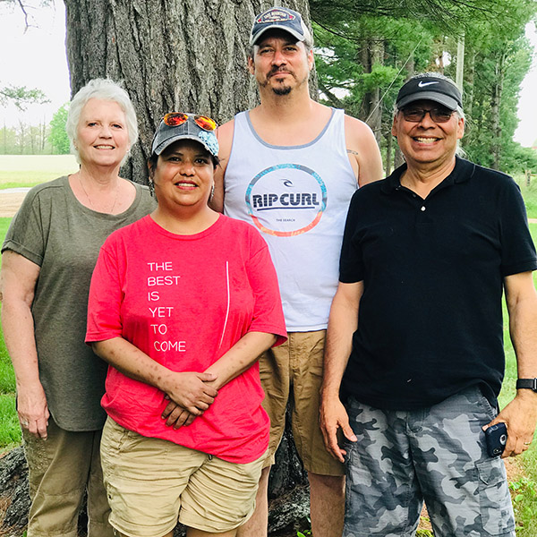 Family of four with adult children pose in front of tree