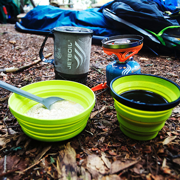 Camping stovepot with bowl of food and coffee mug